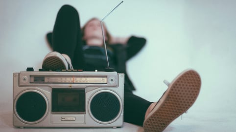 A woman lays on a bed with her foot on a vintage stereo, as she attempts to get over her temp love heartbreak.