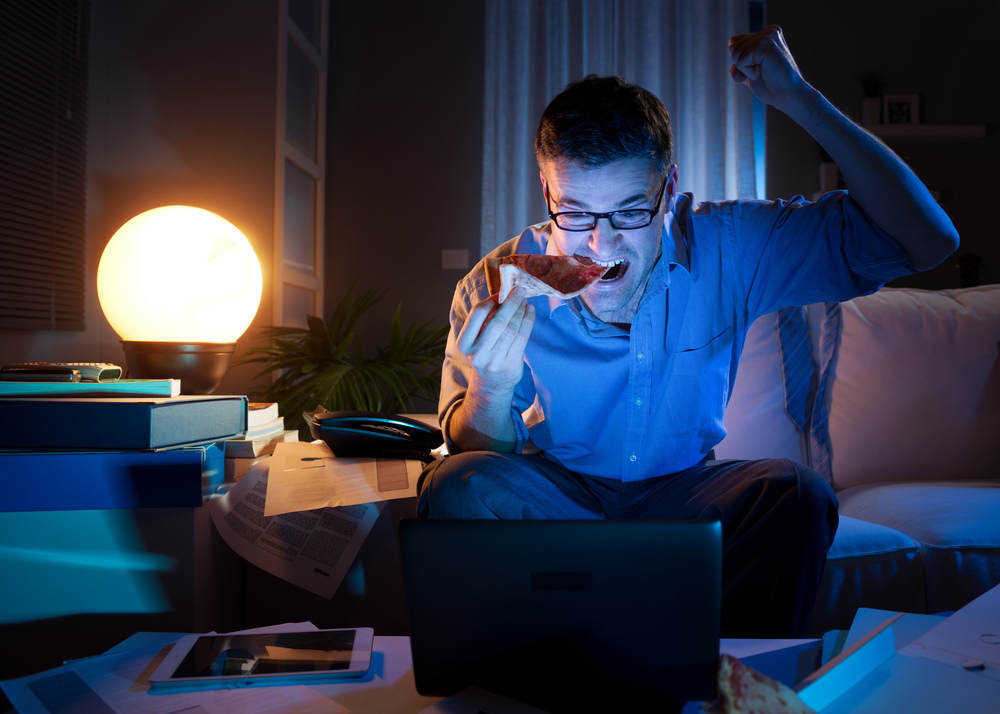 Man watches sports video on laptop while eating pizza.