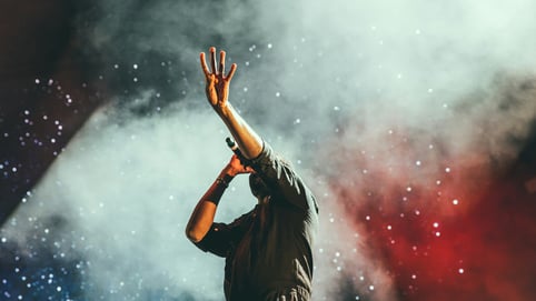 A person performs a popular music song on stage with a backdrop of smoke and stars.