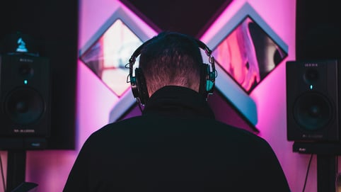 The back of a man's head wearing headphones, sitting between two monitor speakers as he creates his audio branding strategy.